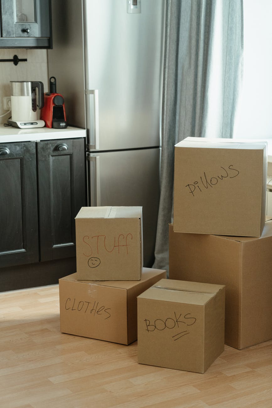 廚房地上堆疊著多個標註「STUFF」「CLOTHES」「BOOKS」「PILLOWS」字樣的搬家紙箱