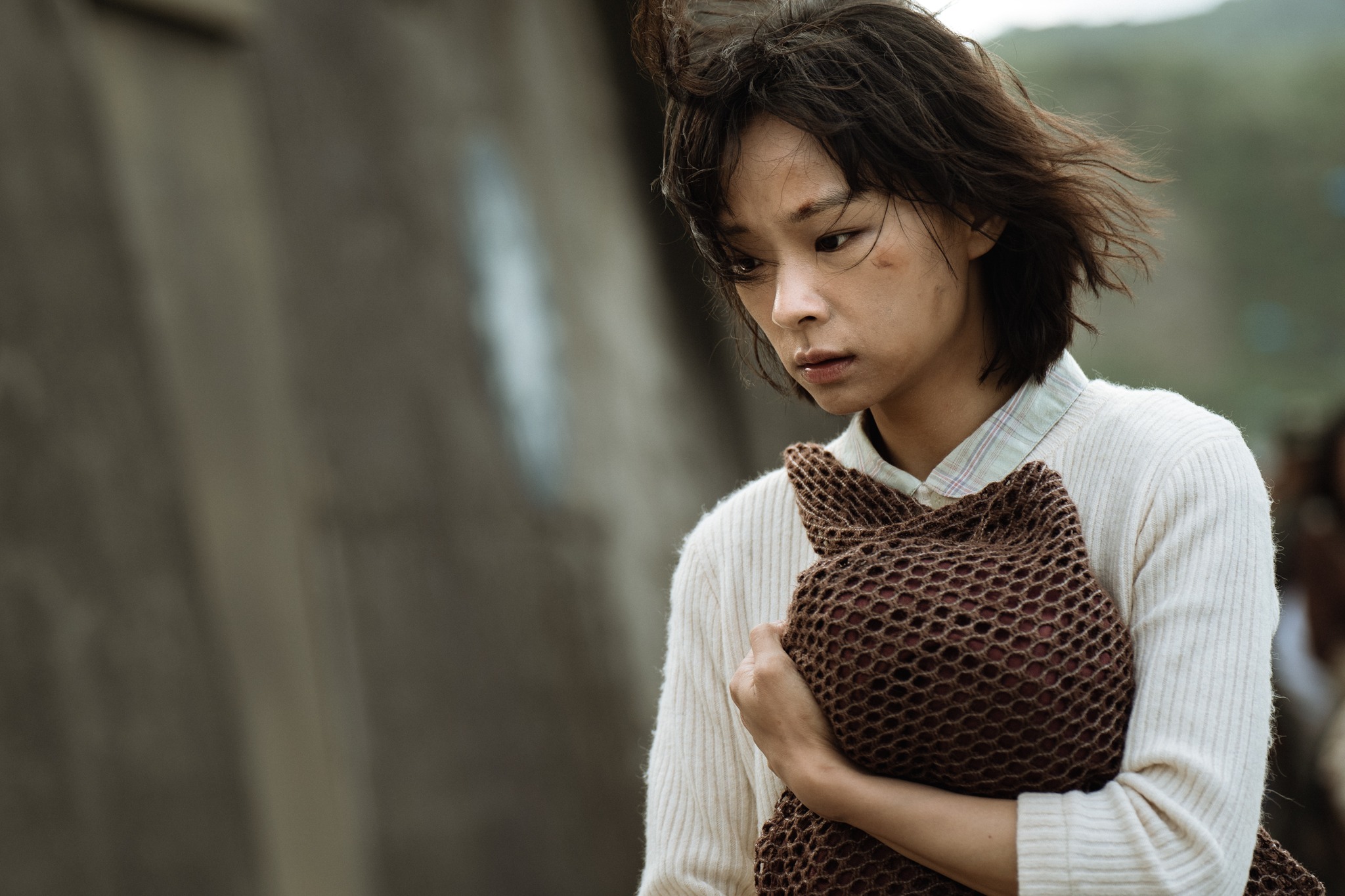電影《流麻溝十五號》劇照:女子懷抱著網袋包裹的物品,神情落寞地低頭走著