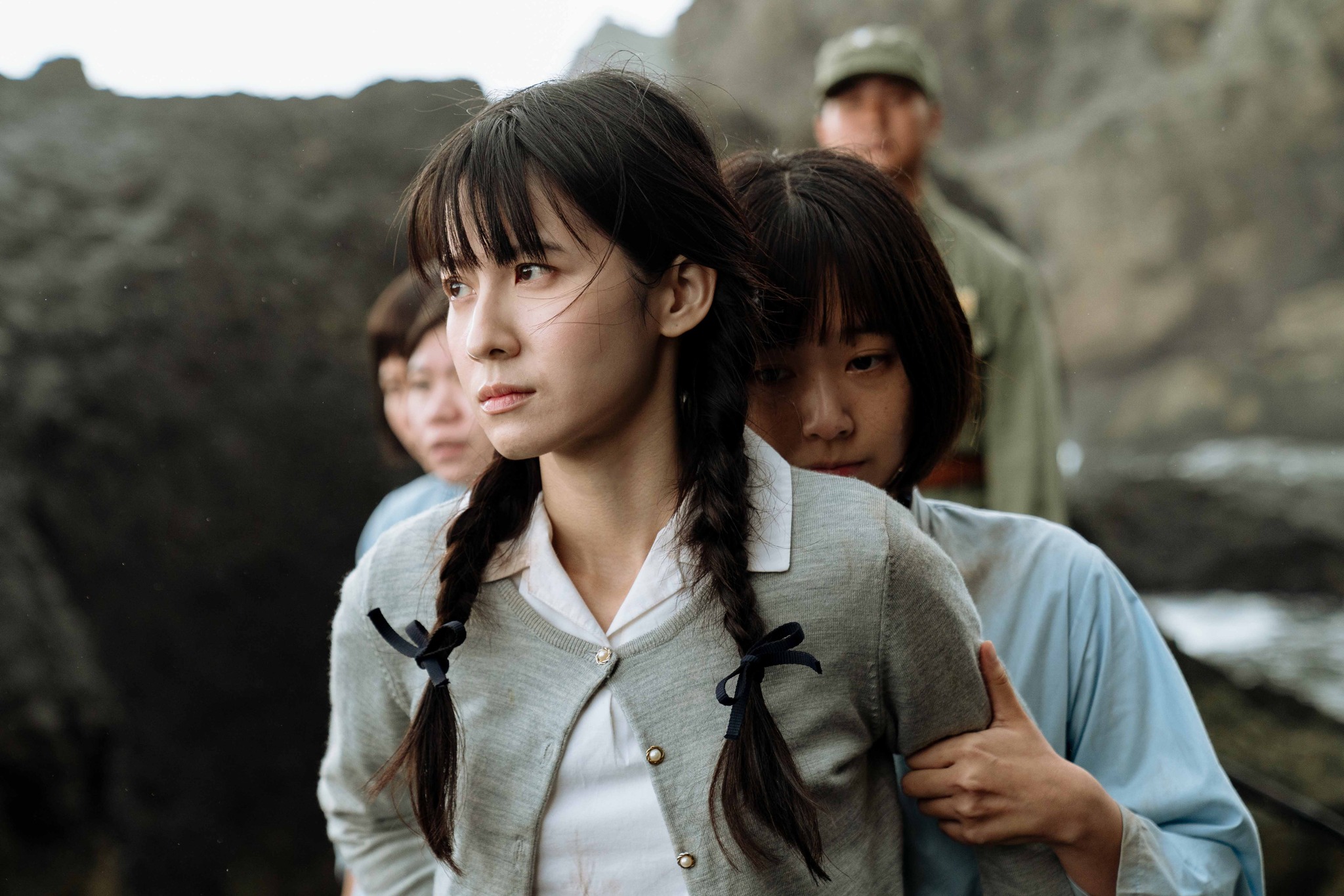 電影《流麻溝十五號》劇照:綁著辮子的女學生被獄卒押解,在岩石地形間行走