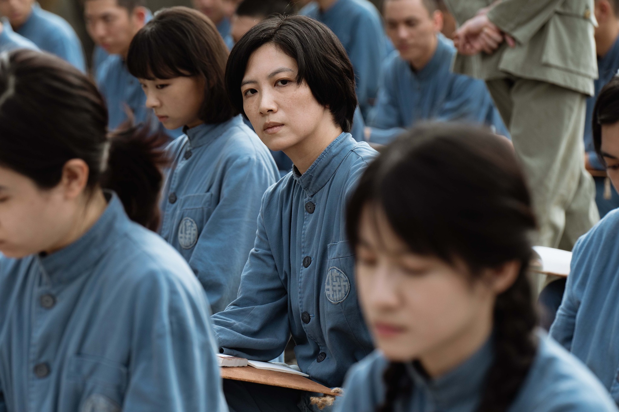 電影《流麻溝十五號》劇照:身穿藍色囚服的女思想犯們坐在教室中,其中一人回頭凝視鏡頭